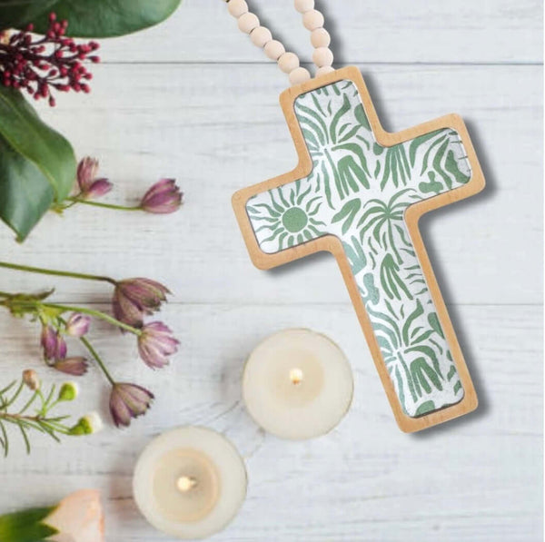 Decorative cross with floral pattern on a white surface with candles and flowers.