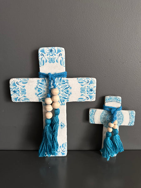 Decorative cross with blue and white pattern and tassels on a dark surface.
