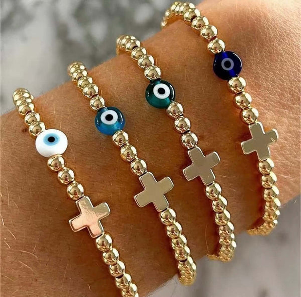 Gold beaded bracelet with evil eye and cross charms on a wrist.